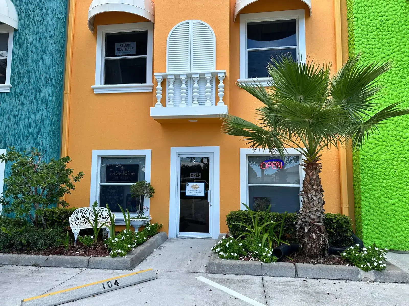 The showroom from the parking lot: an orange two-story building with a white balcony; Suite 104 is the center glass door on the ground floor, with 104 painted on the curb.